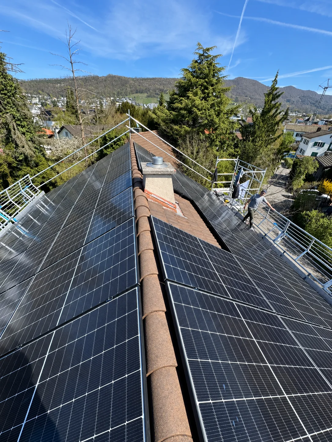 Blick über Solarmodule entlang des Dachfirsts mit einem Kamin